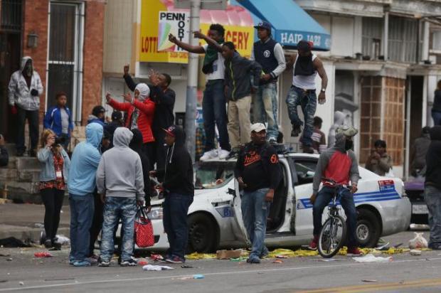 Demonstrators standing on top of a destroyed police vehicle during violent protests following the funeral of Freddie Gray April 27th 2015 (Getty Images)